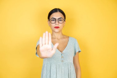 Sarı arka planda duran gözlüklü güzel bir kadın avucunun içi gibi şarkı söylemeyi kesiyor..