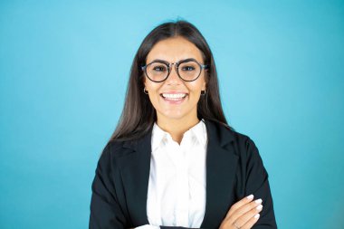 İzole edilmiş mavi arka planda genç ve güzel bir iş kadını kollarını kavuşturup gülümseyen kameraya bakıyordu.