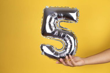 Beş numaralı balonu tutarak izole edilmiş sarı arka planı teslim et.