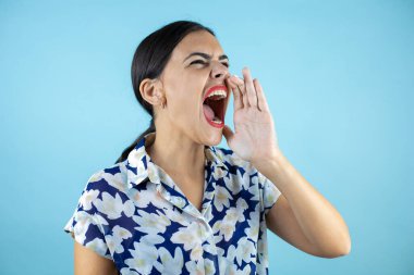 Genç, güzel bir kadın, izole edilmiş mavi arka planda avazı çıktığı kadar bağırıyor ve bağırıyor.