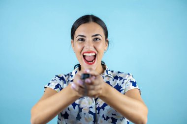 Genç ve güzel bir kadın mavi arka planda dikilip düğmeye basıyor..