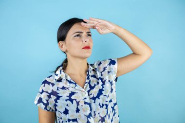 Genç ve güzel bir kadın mavi arka planda duruyor. Uzaklarda bir şey arıyor..