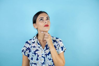 Genç, güzel bir kadın mavi arka planda duruyor. Kendine güvenen, kollarını kavuşturmuş ve çenesini kaldırmış gülümseyen bir kadın..