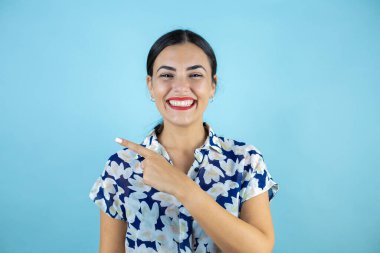 İzole edilmiş mavi arka planda duran genç ve güzel bir kadın kameraya bakıp tek parmağıyla boşluğu işaret ediyor..