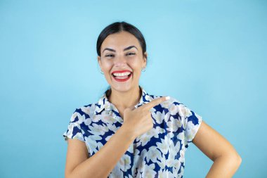 İzole edilmiş mavi arka planda duran genç ve güzel bir kadın kameraya bakıp tek parmağıyla boşluğu işaret ediyor..