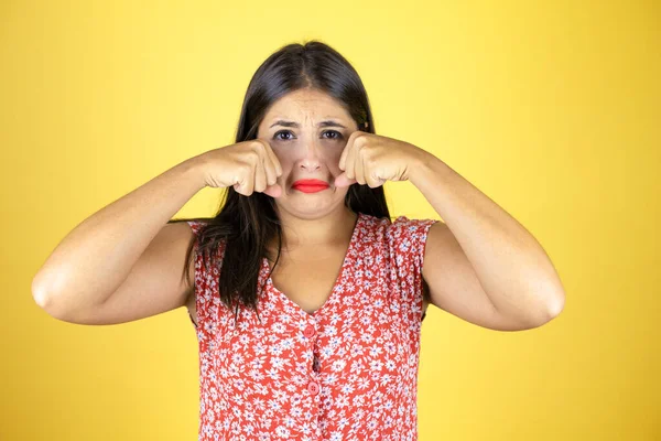 Genç ve güzel bir kadın, izole edilmiş sarı arka planda depresif ve endişeli, sinirli ve korkmuş bir şekilde ağlıyor. Üzücü ifade.