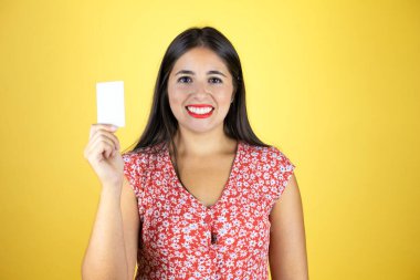 Genç ve güzel bir kadın, izole edilmiş sarı arka planda gülümsüyor ve beyaz kart gösteriyor.