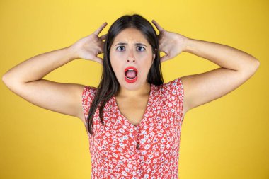 Genç, güzel bir kadın, izole edilmiş sarı arka planda. Şaşırmış ve korkmuş.