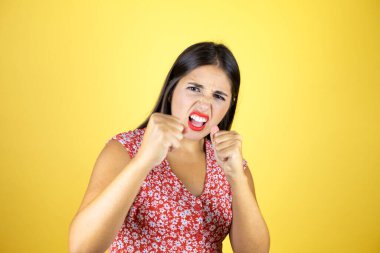 Genç, güzel bir kadın, sarı arka planda. Yumruk yumruğa dövüşme, agresif ve öfkeli saldırı, tehdit ve şiddet.