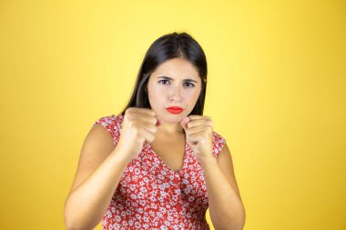 Genç, güzel bir kadın, sarı arka planda. Yumruk yumruğa dövüşme, agresif ve öfkeli saldırı, tehdit ve şiddet.