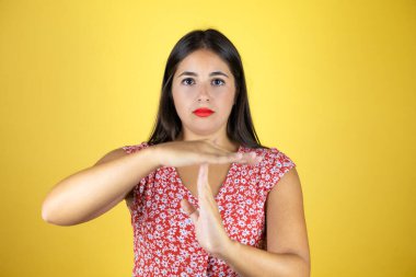 Soyutlanmış sarı arka planda genç, güzel bir kadın. Elleriyle jest yapıyor, hayal kırıklığına uğramış ve ciddi bir yüz ifadesi var.