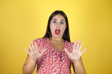 Sarı arka planda yaşayan genç ve güzel bir kadın. Korkudan dehşete düşmüş ve korkmuş. El hareketlerini durdur, şok içinde bağır. Panik konsepti.