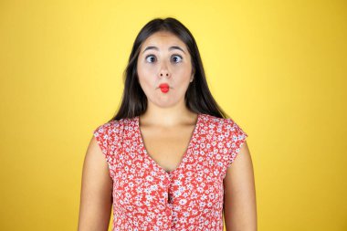 Genç ve güzel bir kadın, izole edilmiş sarı arka planda, dudaklarıyla balık yüzü yapıyor, çılgınca ve komik bir jest..