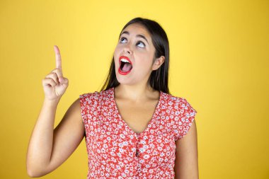 Soyutlanmış sarı arka planda genç ve güzel bir kadın şaşırmış, işaret ediyor ve bakıyor..
