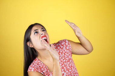 Genç, güzel bir kadın, izole edilmiş sarı arka planda. Kolları yukardan düşen bir şey gibi korkmuş.