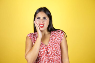 İzole edilmiş sarı arka planda genç bir kadın diş ağrısı ya da diş hastalığından dolayı acı dolu bir ifadeyle dudaklarına dokunuyor.