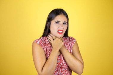 Güzel bir kadın, izole edilmiş sarı arka planda. Ağrılı bir boyuna dokunuyor. Grip, mantar ve enfeksiyon yüzünden boğazı ağrıyor.