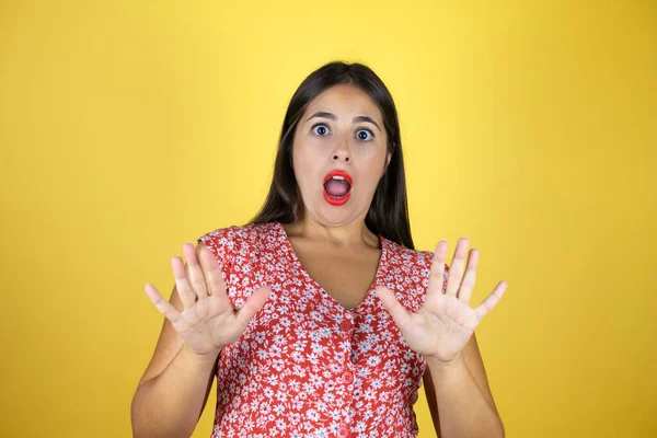 Sarı arka planda yaşayan genç ve güzel bir kadın. Korkudan dehşete düşmüş ve korkmuş. El hareketlerini durdur, şok içinde bağır. Panik konsepti.