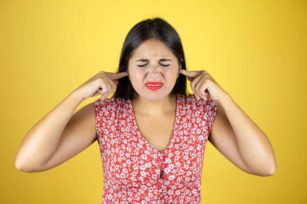 İzole edilmiş sarı arka plan üzerinde genç ve güzel bir kadın yüksek sesli müziğin gürültüsü için parmaklarıyla kulakları kapatıyor. Sağır kavramı.