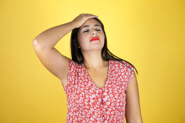 Genç, güzel bir kadın, izole edilmiş sarı arka planda bir elini başının üstüne koyup sanki bir şey unutmuş gibi gülümsüyor.