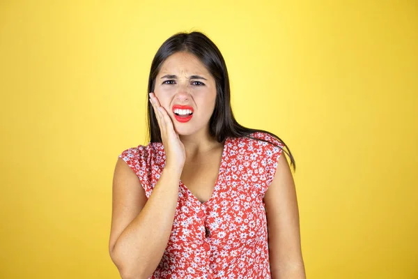 İzole edilmiş sarı arka planda genç bir kadın diş ağrısı ya da diş hastalığından dolayı acı dolu bir ifadeyle dudaklarına dokunuyor.