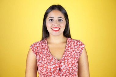 Genç ve güzel bir kadın, izole edilmiş sarı arka planda gülümsüyor ve kameraya bakıyor.