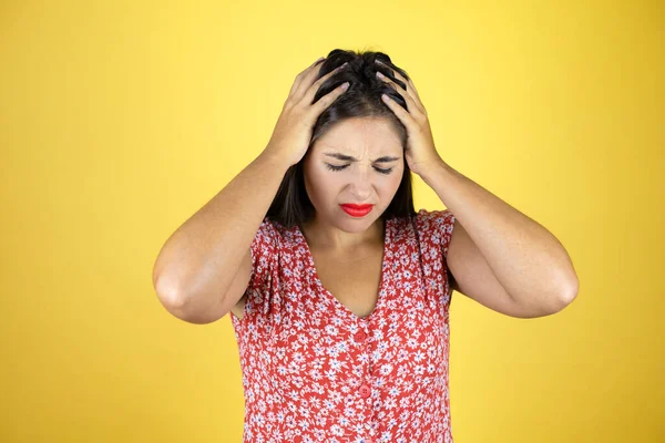 Genç ve güzel bir kadın, sarı arka planda, baş ağrısı, çaresiz ve stresli, çünkü elleri başının üstünde acı ve migren var.
