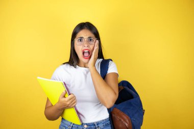 Sırt çantasıyla gezen genç ve güzel bir bayan. Sarı arka planda not defteri tutuyor. Çığlık atıyor ve elleri ağzında şaşırıyor.