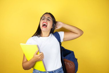 Sırt çantası taşıyan genç ve güzel bir bayan. Sarı arka planda defter tutuyor. Rahatlıyor ve esniyor.
