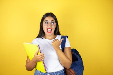 Sırt çantasıyla gezen genç ve güzel bir kız. Elinde not defteri var. Sarı arka planda.