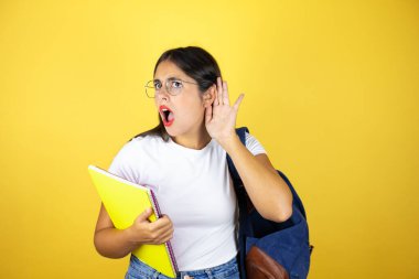Sırt çantasıyla gezen genç ve güzel bir bayan. Sarı arka planda not defteri tutuyor. Kulağından kulağa gelen dedikodulara ve dedikodulara şaşırıyor.