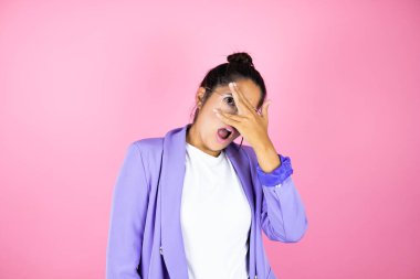Soyutlanmış pembe arka planda genç ve güzel bir iş kadını. Şoka girmiş, yüzünü ve gözlerini kapamış, utanmış bir ifadeyle parmaklarından bakıyor.