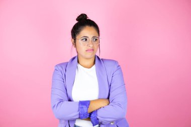 Genç ve güzel bir iş kadını pembe arka planda, çapraz kollardan sıkılmış ve yorgun göründüğünü düşünüyor.