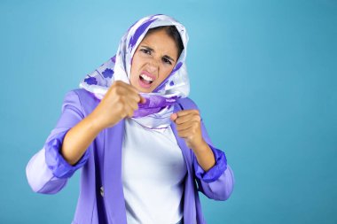 Genç, güzel bir Arap kadın, tecrit edilmiş mavi arka plan üzerine başörtüsü takıyor. Yumruğunu yumrukluyor, saldırıyor, saldırıyor, tehdit ediyor ve şiddet uyguluyor.