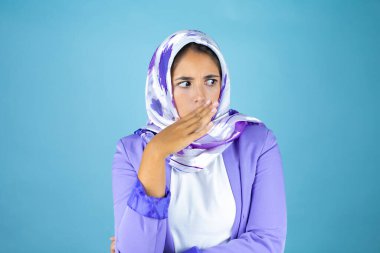 Genç, güzel bir Arap kadın, izole edilmiş mavi arka planda İslami başörtüsü takıyor.