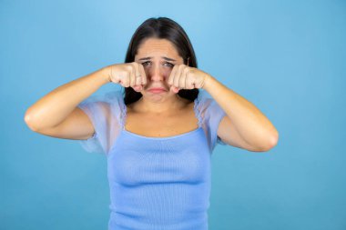 Genç ve güzel bir kadın soyutlanmış mavi arka planda depresif ve endişeli, kızgın ve korkmuş bir şekilde ağlıyor. Üzücü ifade.