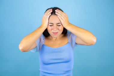 Genç ve güzel bir kadın, izole edilmiş mavi arka planda kulakları, yüksek sesli müziğin gürültüsü için rahatsız edici ifadeleri olan ellerle kapatıyor. Sağır kavramı.