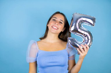 İzole edilmiş mavi arka planı olan genç ve güzel bir kadın gülümseyerek beş numarayı tutuyor. Kutlama konsepti
