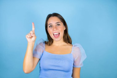 Soyutlanmış mavi arka planı olan genç ve güzel bir kadın parmaklarıyla kafasında bir fikri olduğunu sanarak şaşırdı..