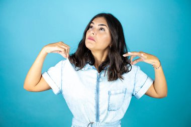 İzole edilmiş mavi arka planda kot pantolon giyen güzel bir kadın başarılı bir ifadeyle..