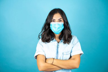 İzole edilmiş mavi arka plan kolları üzerinde tıbbi maske takan güzel bir kadın. Coronavirüs