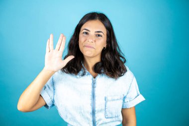 İzole edilmiş mavi arka planda kot pantolon giyen güzel bir kadın Star Trek ucube sembolü yapıyor..