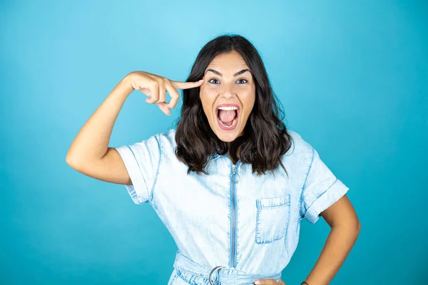 Young beautiful woman wearing a denim jumpsuit over isolated blue background smiling and thinking with her fingers on her head that she has an idea.