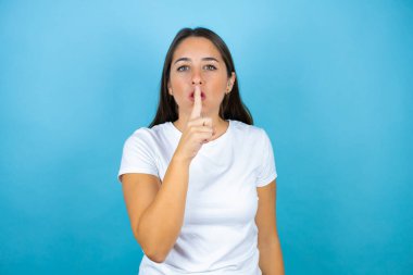 Soyutlanmış mavi arka planda genç ve güzel bir kadın sessiz olmak istiyor. Sessizlik ve gizli konsept.