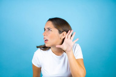 Soyutlanmış mavi arka plan üzerinde genç ve güzel bir kadın kulağından girip kulağına gelen dedikoduları ya da dedikoduları dinleyerek şaşırdı.