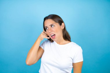 Soyutlanmış mavi arka planda genç ve güzel bir kadın telefon hareketlerini telefonla konuşmak gibi el ve parmaklarıyla yapıyor.