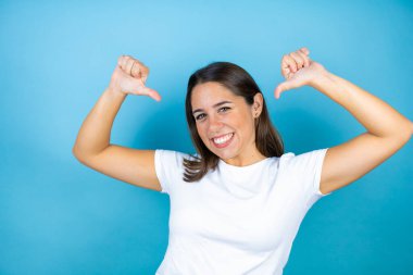 Genç ve güzel bir kadın, soyutlanmış mavi arka planda, kendine güvenen, yüzünde bir gülümsemeyle, kendini gururlu ve mutlu olarak gösteriyor..