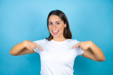 Genç ve güzel bir kadın, soyutlanmış mavi arka planda, kendine güvenen, yüzünde bir gülümsemeyle, kendini gururlu ve mutlu olarak gösteriyor..