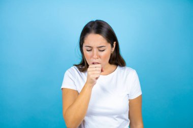 Genç ve güzel bir kadın mavi arka planda, eli ağzında, çünkü öksürüyor.