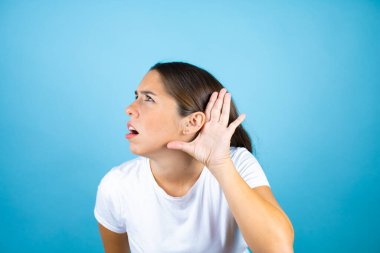 Soyutlanmış mavi arka plan üzerinde genç ve güzel bir kadın kulağından girip kulağına gelen dedikoduları ya da dedikoduları dinleyerek şaşırdı.